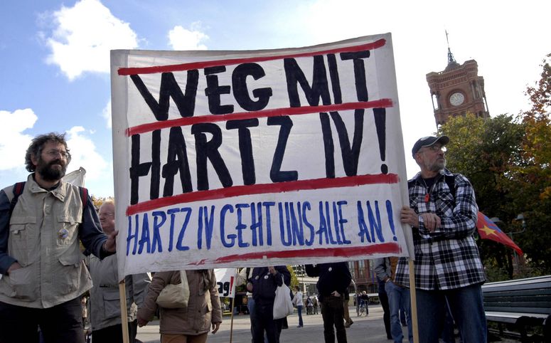 Foto mit zwei Männern, die ein Banner halten, auf dem steht: "Weg mit HartzIV! HartzIV geht uns alle an!"