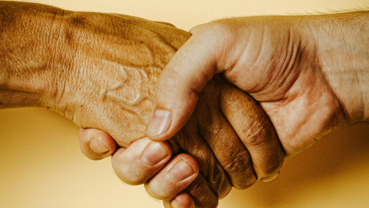 Die Hand einer jungen Person hält die sichtbar viel ältere Hand eines alten Menschen.