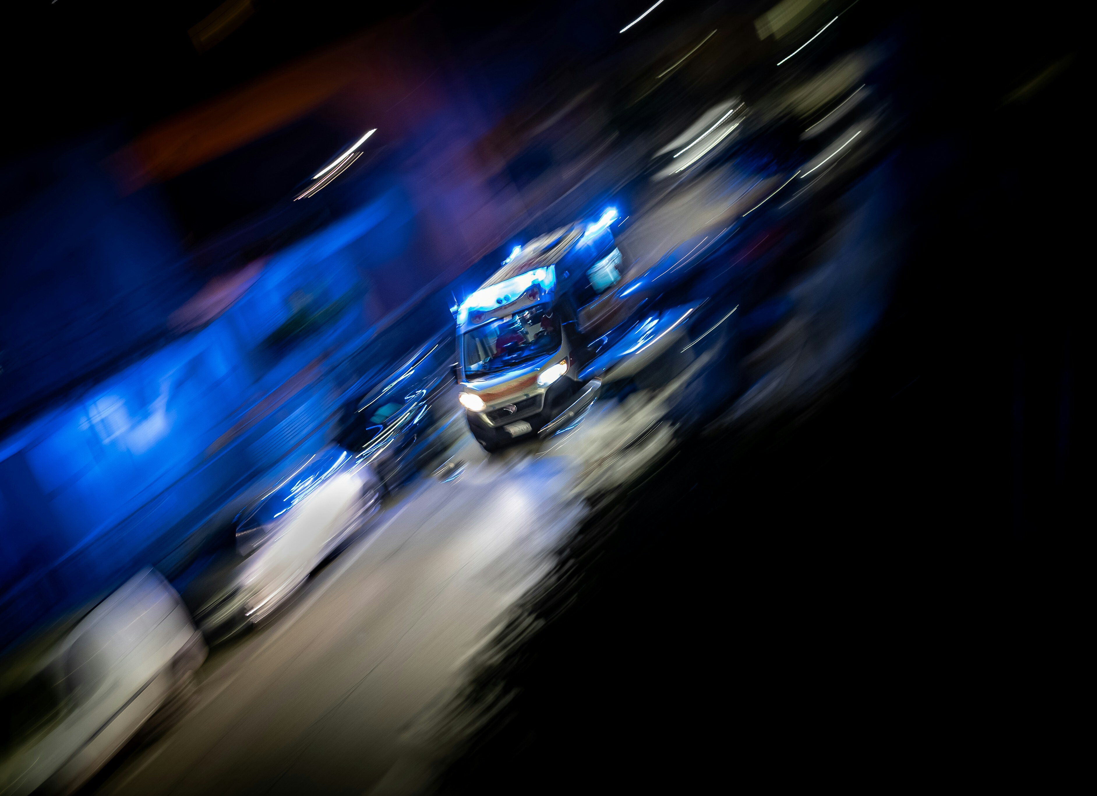 Foto eines Rettungswagens der mit hoher Geschwindigkeit und Blaulicht durch eine Straße fährt.