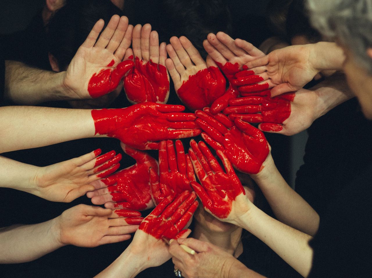 Viele Menschen halten ihre Hände nebeneinander und darauf ist ein großes rotes Herz gemalt.