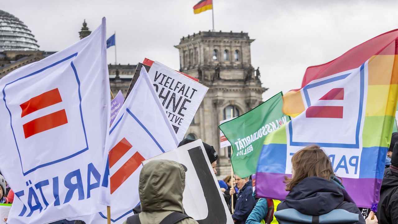 Vor dem Reichstag wehen viele Paritätische Fahnen auf einer Demo, darunter eine Regenbogenfahne.