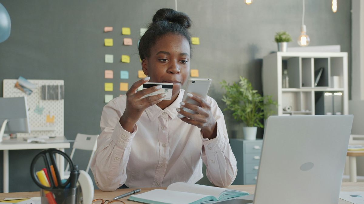 Eine Frau sitzt vor einem Laptop mit Kreditkarte und Smartphone