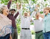 Das Bild zeigt fünf ältere Menschen unterschiedlicher Herkunft die lächelnd die Arme in die Luft werfen und dabei in einem Halbkreis stehen