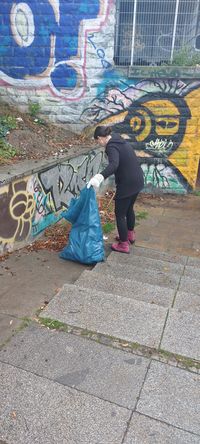 Das Bild zeigt eine Frau, die an einer Treppe Müll sammelt