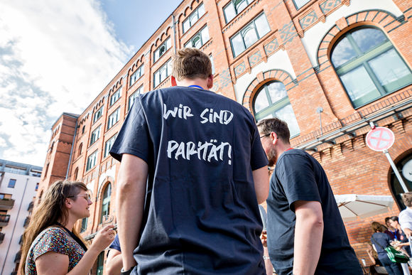 Rückenansicht unseres Scout-T-Shirts mit Aufdruck "Wir sind Parität" vor der Hausfront der Neuen Mälzerei in Berlin