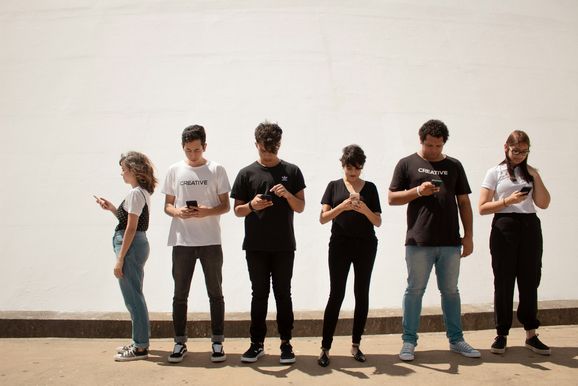 6 stehende Personen in einer Reihe, die sich mit ihrem Smartphone beschäftigen