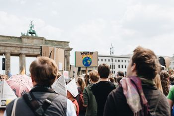 Menschen demonstrieren vor dem Brandenburger Tor. Auf einem Schild ist ein brennender Erdball zu sehen und die Worte "Wake Up"