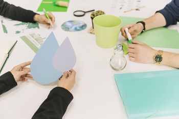 Das Bild zeigt die Hände von drei Personen, die an einem Tisch sitzen und an Ideen für ökologische Projekte arbeiten.