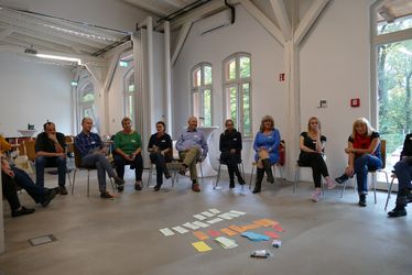 Workshopteilnehmer*innen sitzen im Kreis, auf dem Boden Karteikarten.