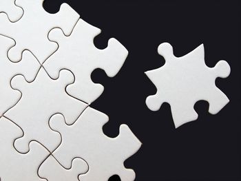 Weißes Puzzle vor schwarzem Hintergrund, ein Teil außerhalb des Puzzels.