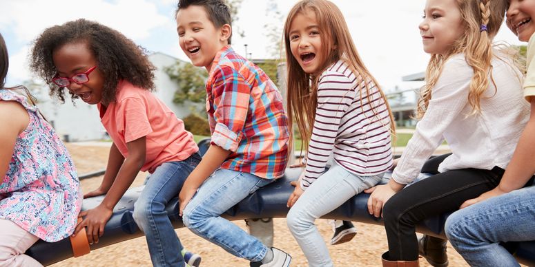 Viele unterschiedliche Kinder unterschiedlichen Alters drehen sich lachend auf einem Spielgerät auf einem Spielplatz.