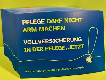 Blaue Postkarten vor grünem Hintergrund. Auf der Vorderseite der Postkarten ist zu lesen: Pflege darf nicht arm machen - Vollversicherung in der Pflege, jetzt!