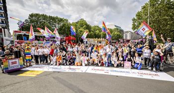 Auf dem Bild sind etwa 50 Personen zu sehen, die auf der Straße hinter einem liegenden Banner stehen, auf dem "Vielfalt, Offenheit, Toleranz" steht. Einige schwenken Regenbogen-Fahnen mit dem Logo des Paritätischen.