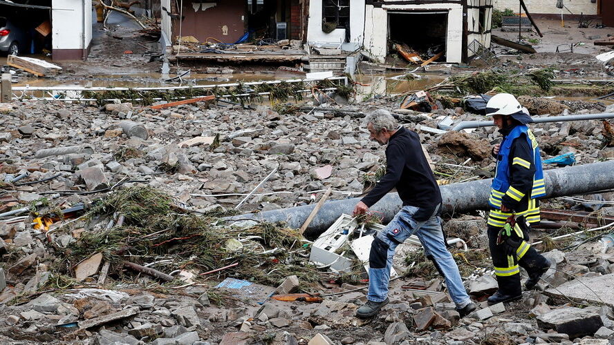Zwei Männer lauen durch eine Trümmerlandschaft in einem Überflutungsgebiet