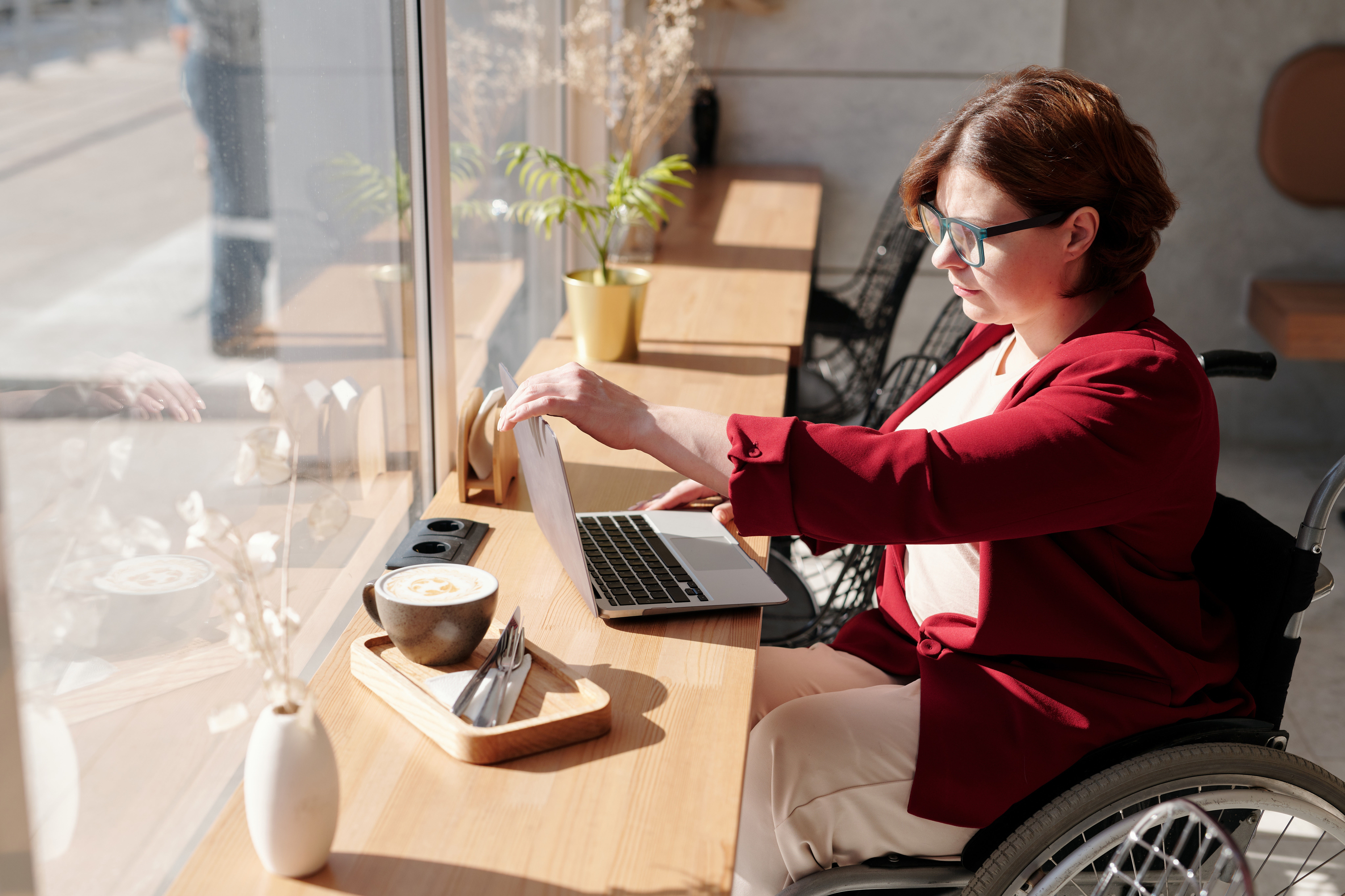 Eine Frau im Rollstuhl sitzt in einem Café an einem Laptop.