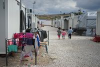 Blick zwischen provisorische Containerhäuser eines Flüchtlingscamps, in dem drei Kinder von hinten zu sehen sind.