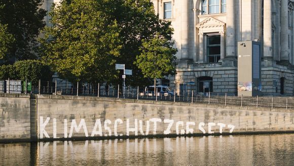 Der Bundestag, auf einer Mauer steht, halb überflutet von einem Fluss: "Klimaschutzgesetz"