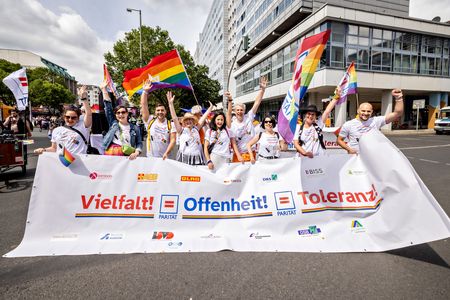 Vieen Menschen mit Regenbogenfahnen auf einer Demo, die ein Transparent halten, auf dem steht: Vielfalt, Offenheit, Toleranz.
