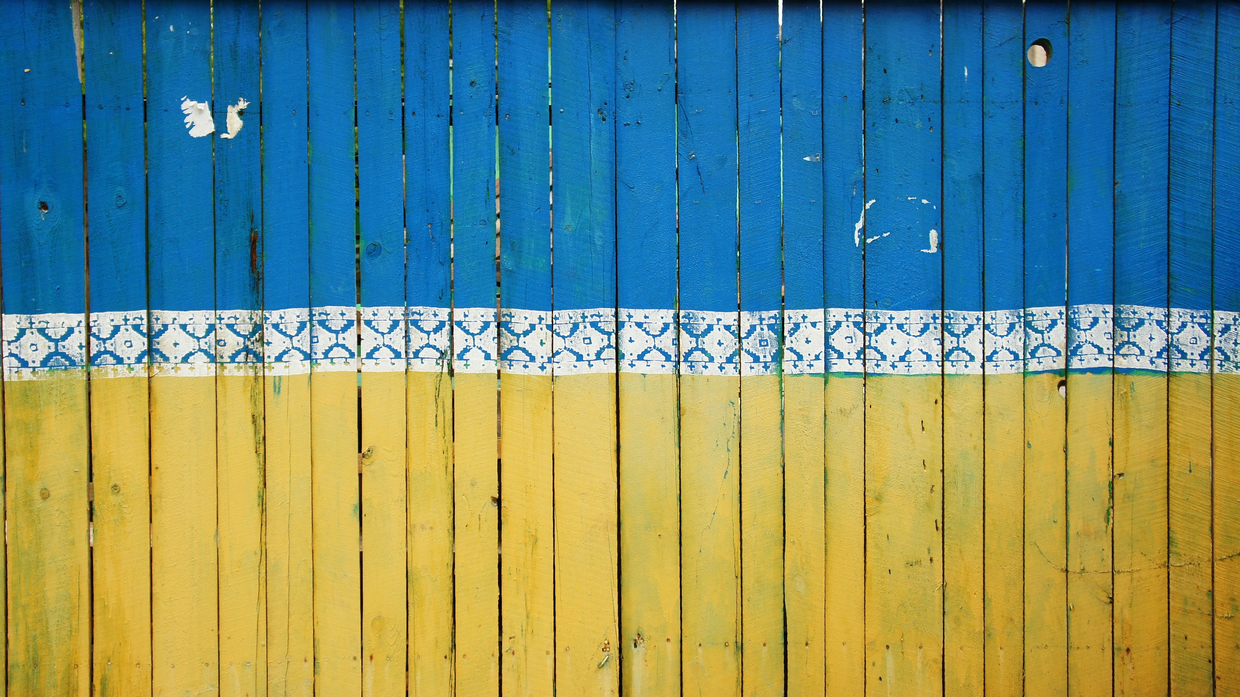 Zu sehen ist ein Holzzaun, der in den Farben der Ukraine gestrichen ist.