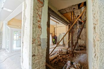 Einblick in ein Haus, das gerade renoviert wird. Zu sehen sind nackte Steinwände und eine Person, die auf einer Leiter steht.