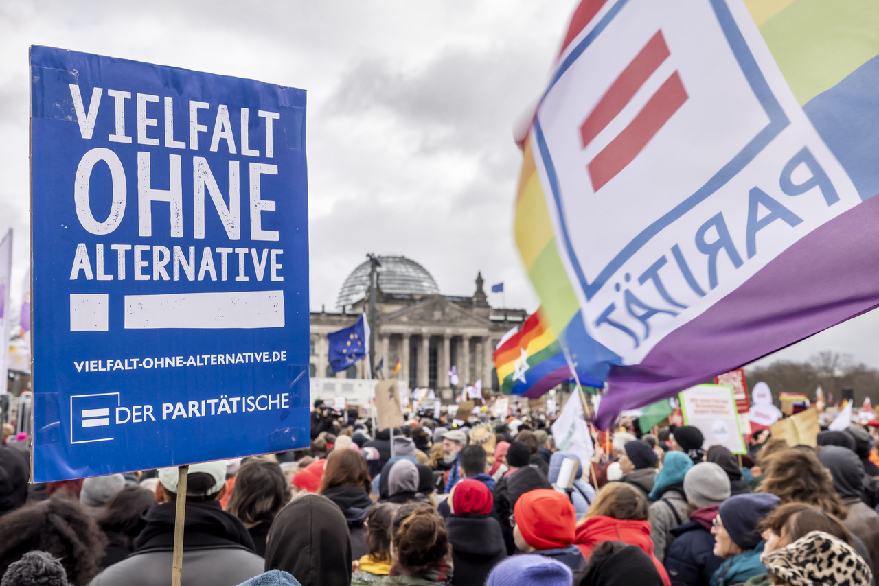 Vor dem Reichstag ist in einer riesigen Menschenmenge ein Schild zu sehen, auf dem steht "Vielfalt ohne Alternative!". Daneben eine Fahne in Regenbogenfahne mit dem Logo des Paritätischen Wohlfahrtsverbandes.