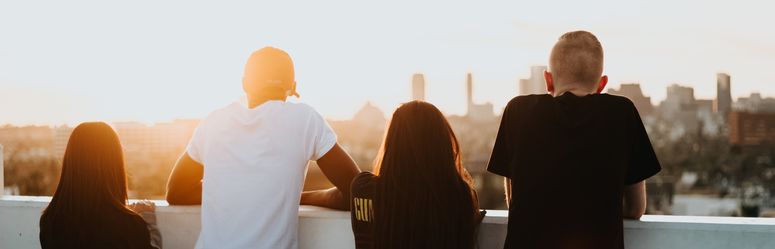 Vier Jugendliche schauen über eine Stadt in Richtung Sonne