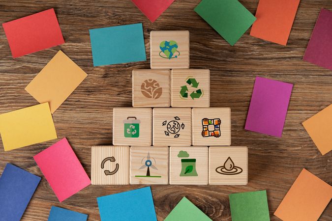 In der Mitte sind Holzwürfel auf denen Nachhaltigkeitssymbole wie Windkraft oder Recycling abgebildet sind. Außemrum liegen bunte Steine in Farben der SDGs. 