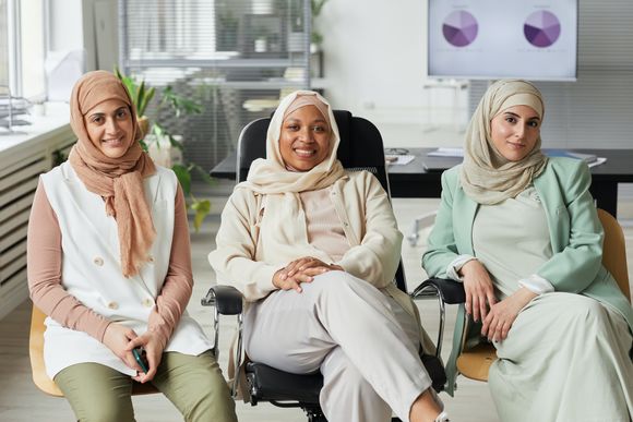 Drei Frauen mit Kopftuch sitzen in einem Büro nebeneinander und lächeln. 