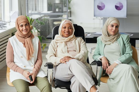Drei Frauen mit Kopftuch sitzen in einem Büro nebeneinander und lächeln.
