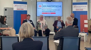Eine weitere Podiumsrunde mit vier sitzenden Diskussionsteilnehmenden, gefilmt über die Schulter einer im Vordergrund sitzenden Person aus dem Publikum.