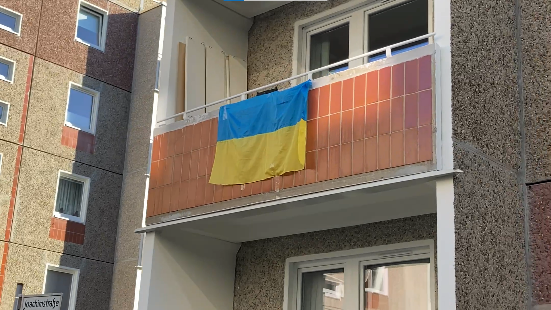 An einem Balkon in einem Plattenbaugebiet hängt eine Ukraine-Flagge