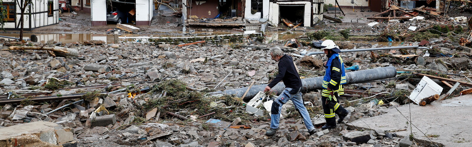 Zwei Männer lauen durch eine Trümmerlandschaft in einem Überflutungsgebiet