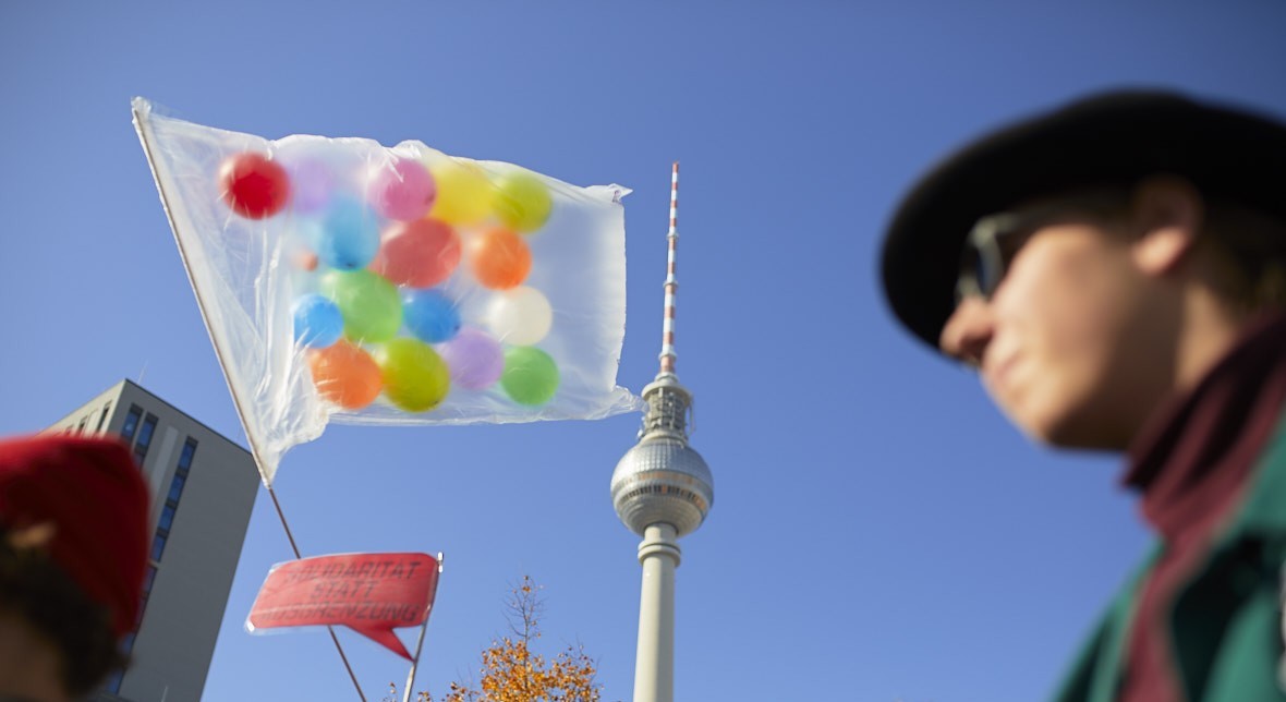 Eine Fahne mit vielen bunten Luftballons weht vor dem Fernsehturm, davor laufen Menschen.